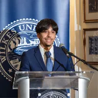 Nathaniel Martes speaking at a Wilkes University podium, lightly pixelated.