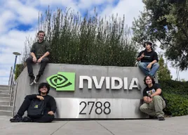 Four people gathered around the NVIDIA campus sign, lightly pixelated.